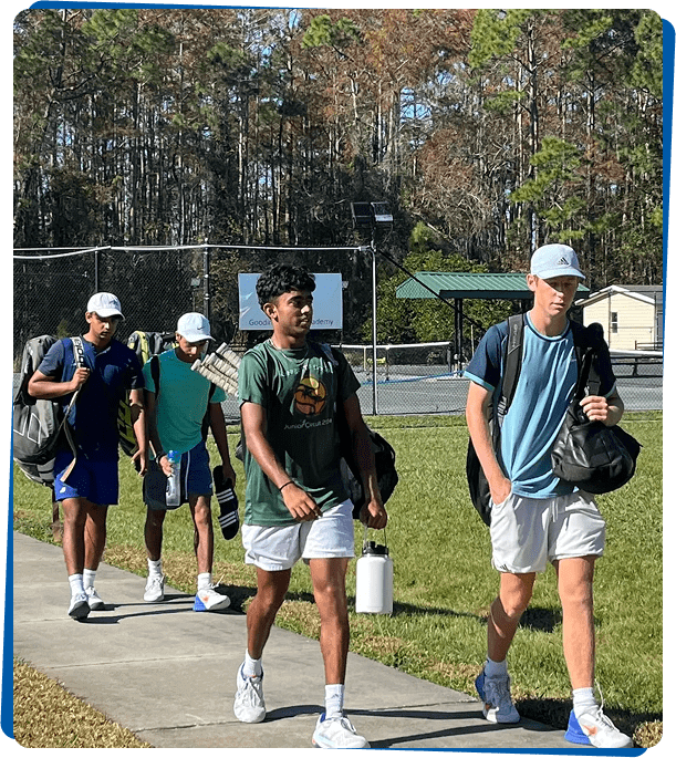 Four tennis players walking on sidewalk.