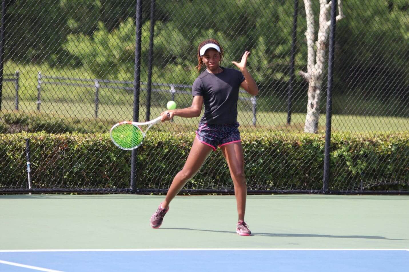 Woman playing tennis on an outdoor court, hitting a forehand.