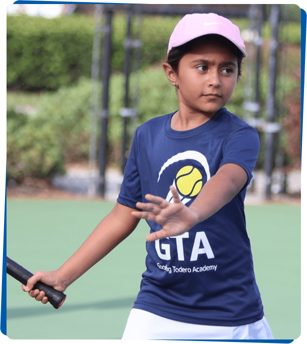 Boy in a blue shirt holding a tennis racket on a court.