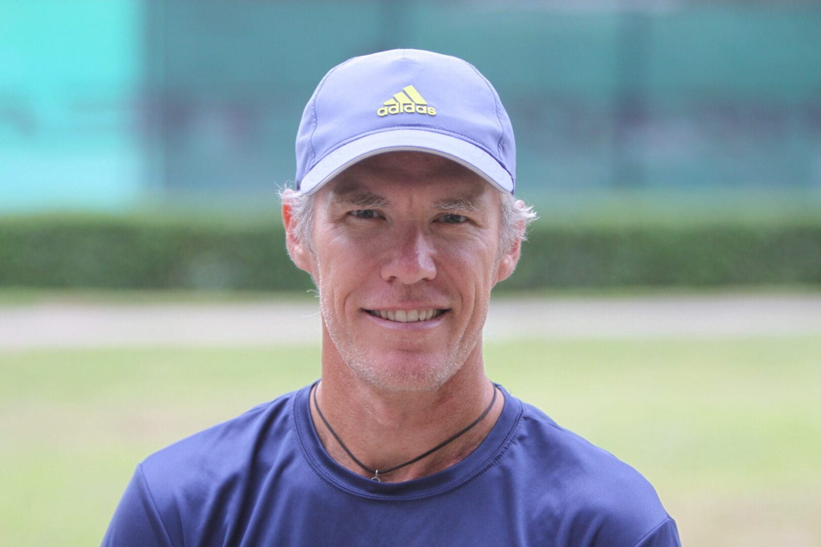 Smiling man wearing a blue cap and navy shirt outdoors.