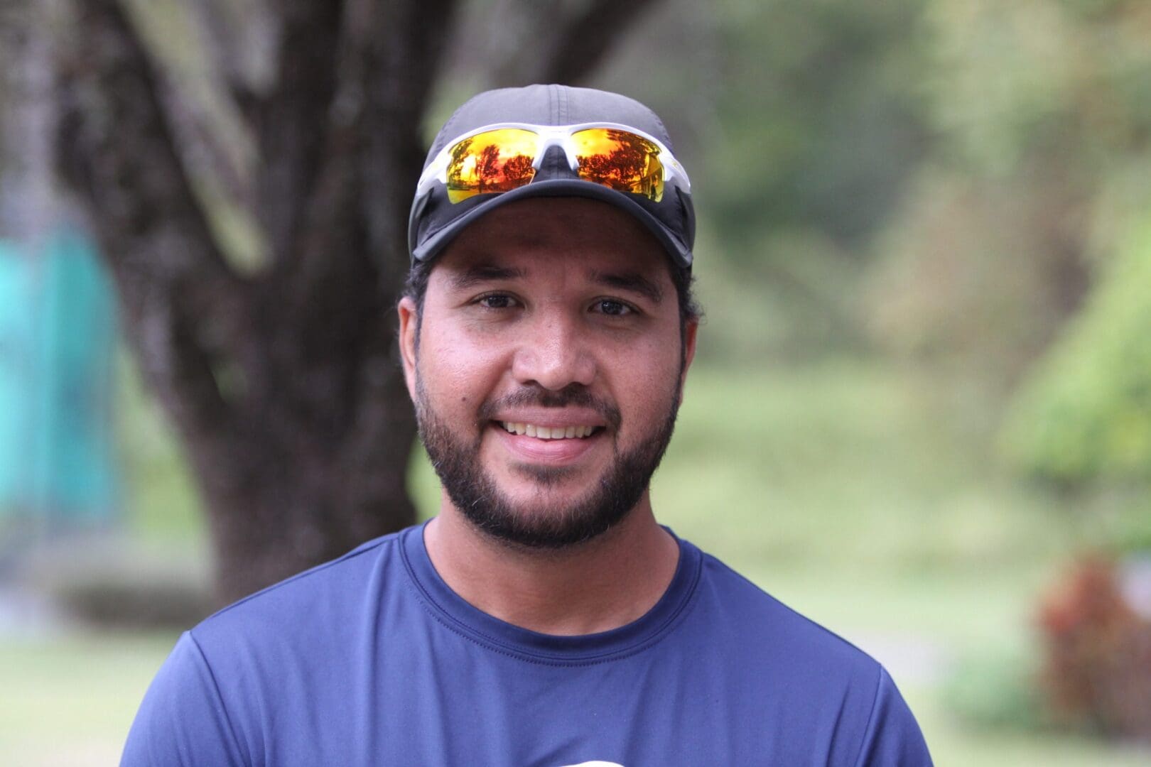 Smiling man wearing a cap and sunglasses on his head.