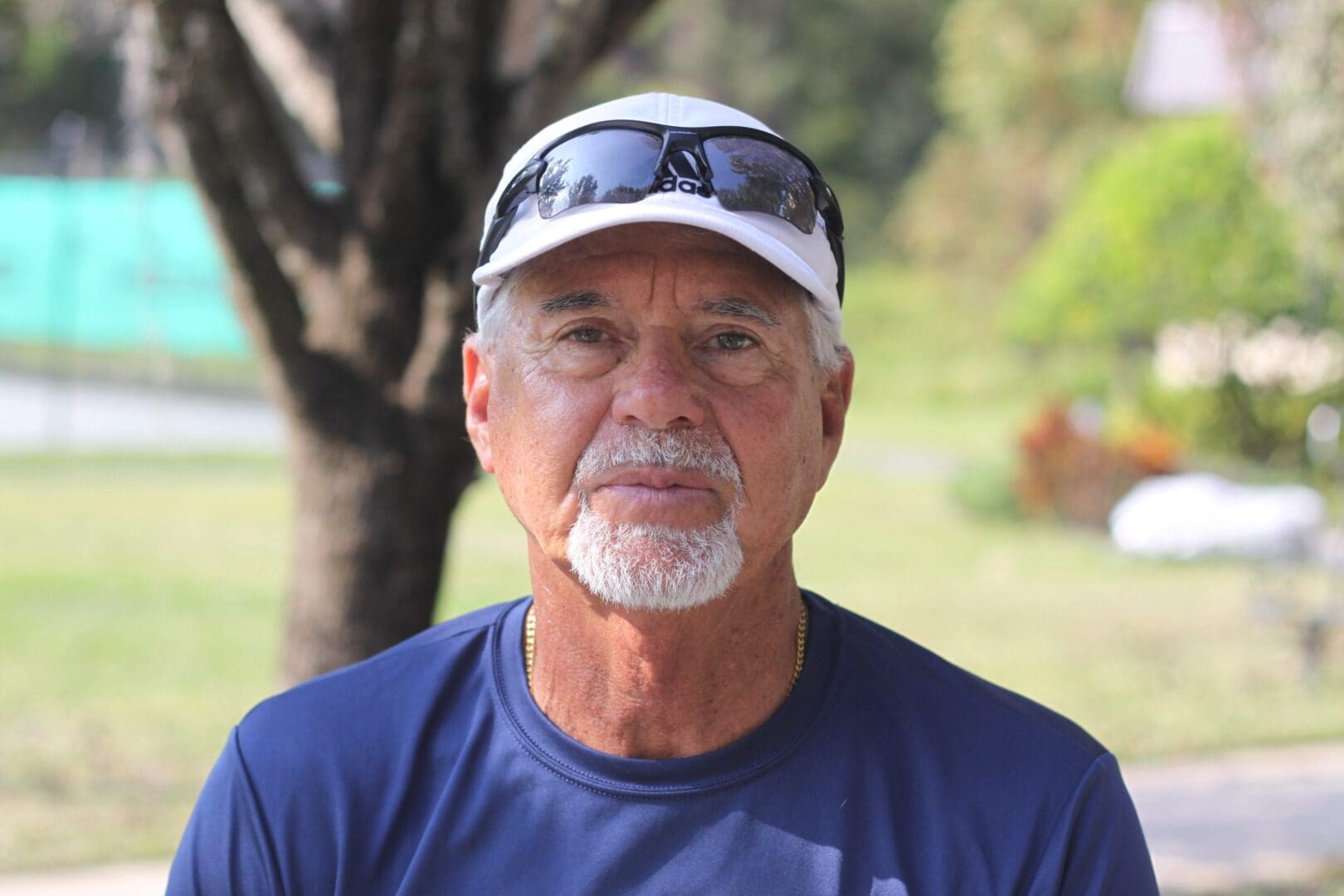 Portrait of an elderly man outdoors wearing a cap and sunglasses.