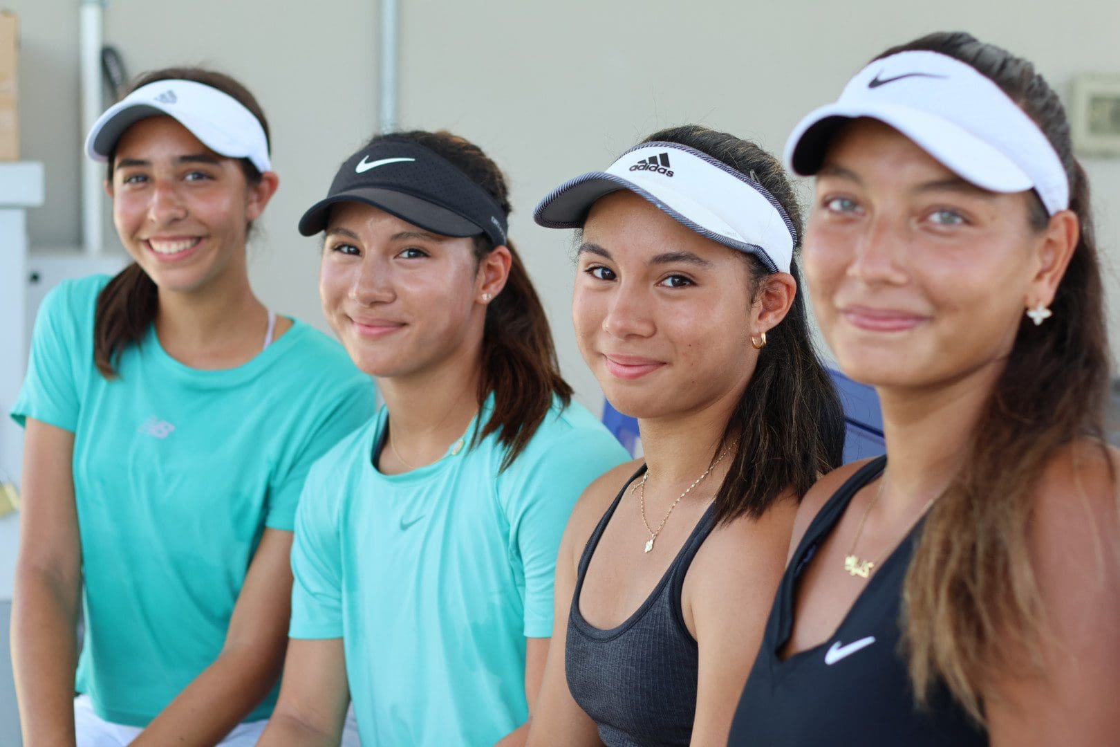 Four young women in sportswear smiling, standing side by side.