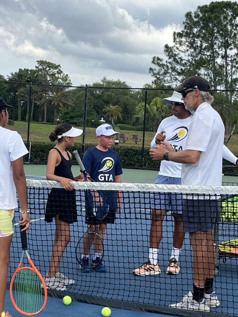 Kids and coaches chatting on a tennis court during practice.