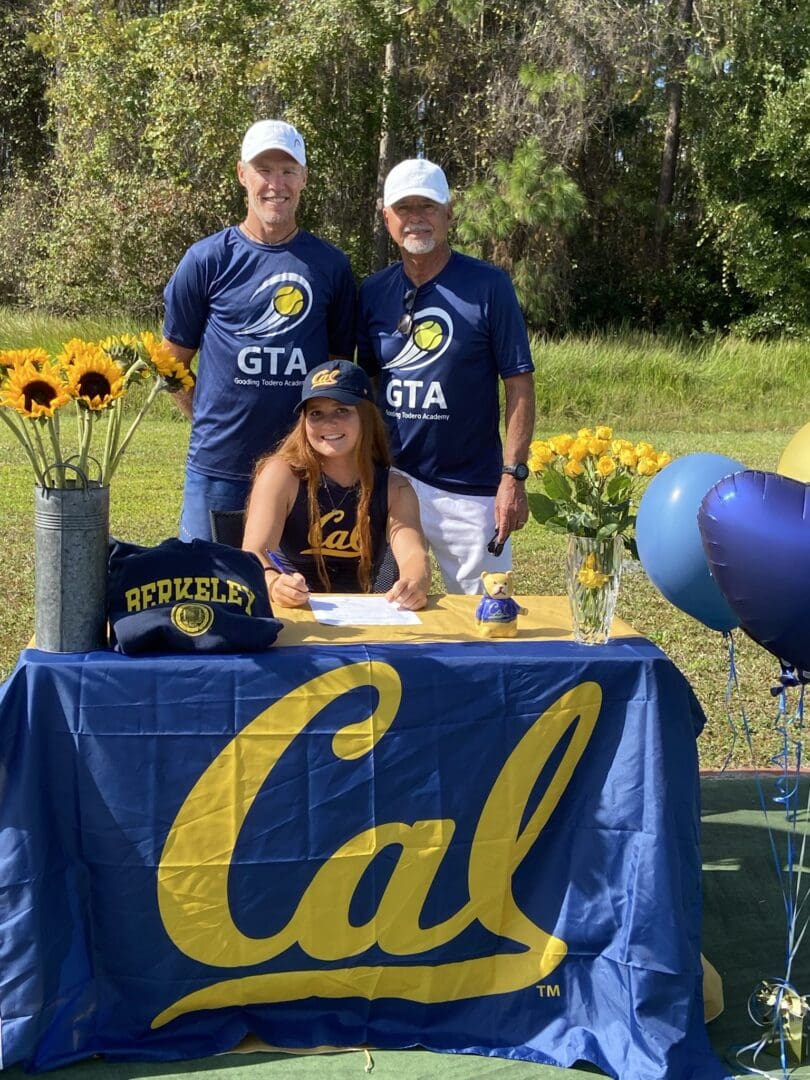 Two men in Cal shirts at a university table with balloons and sunflowers.