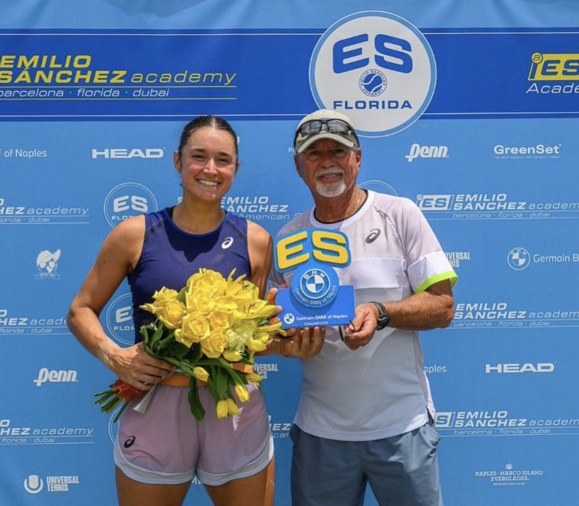 Two smiling tennis players hold a trophy and flowers on a blue event backdrop.
