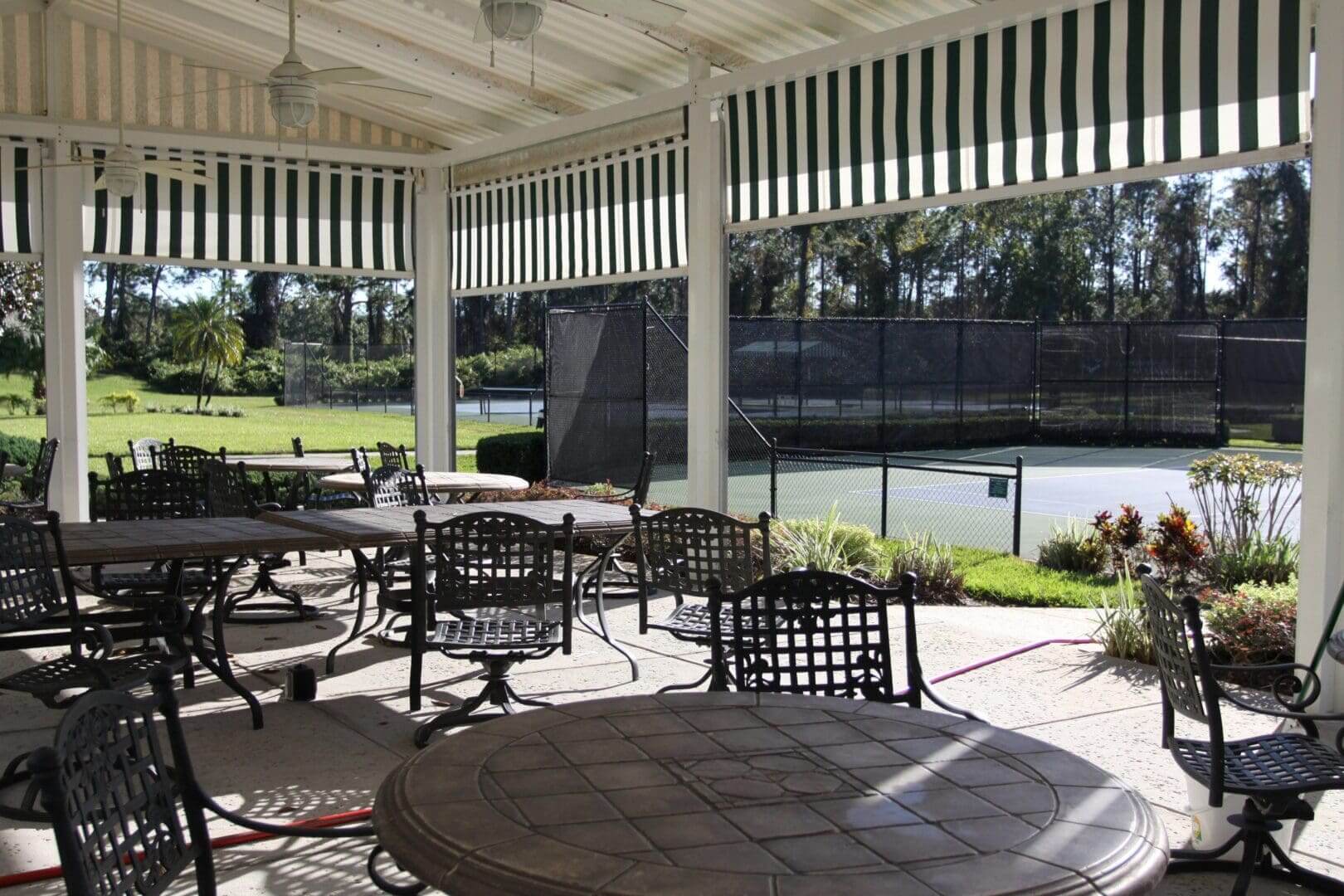 Outdoor seating area by a tennis court with striped awnings.