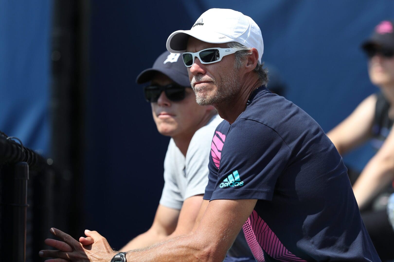Two men wearing caps and sunglasses sitting outdoors.