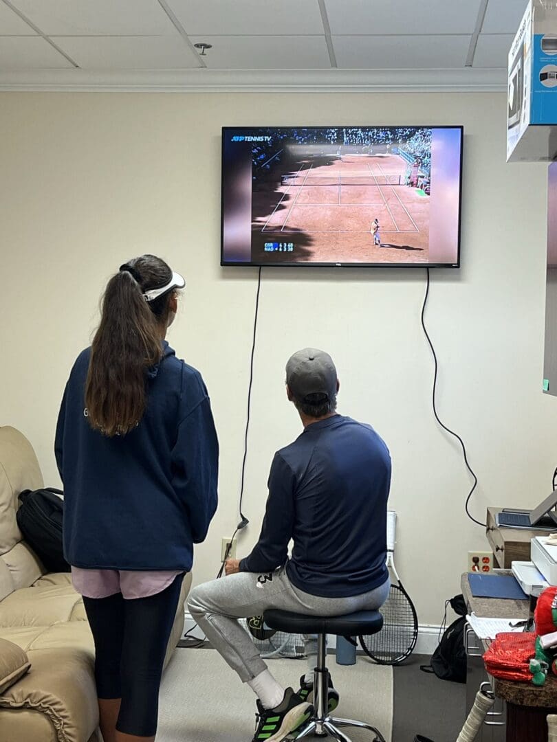 Two people playing a video game on a wall-mounted TV.