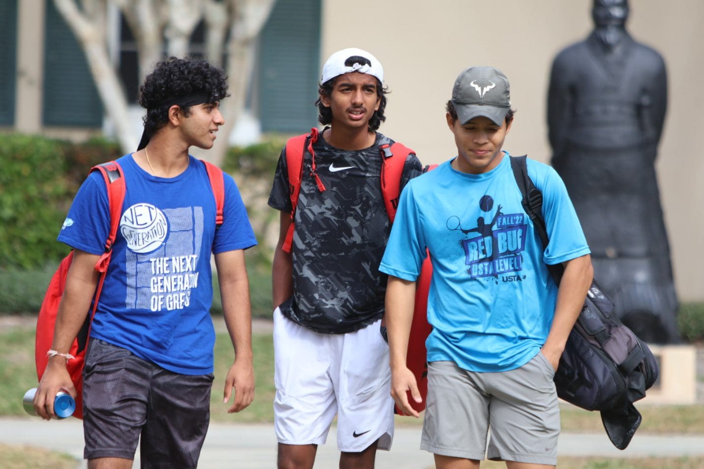 Three young men walking together outdoors, dressed casually.