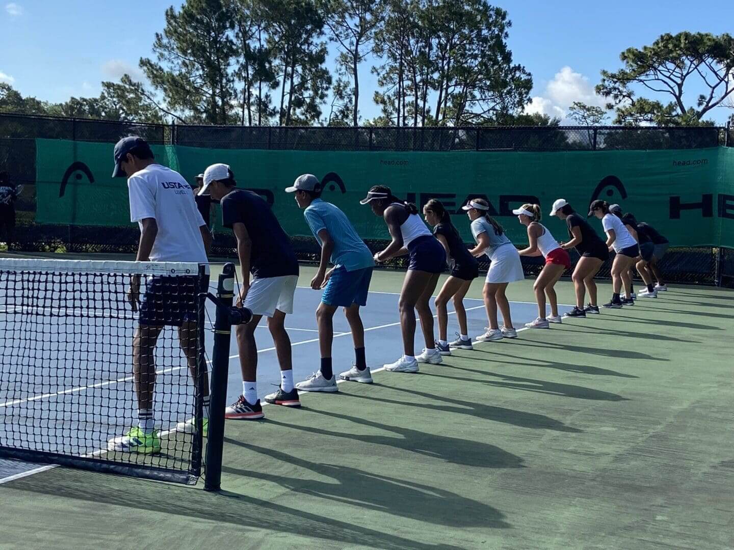 Young tennis players lined up at the net, preparing for practice or a drill.