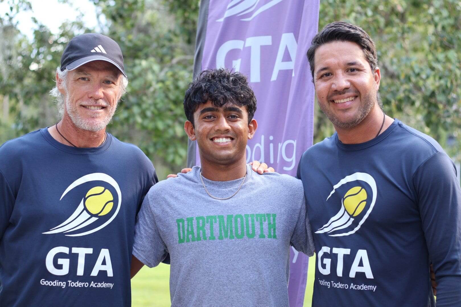 Three men smiling at tennis academy event.