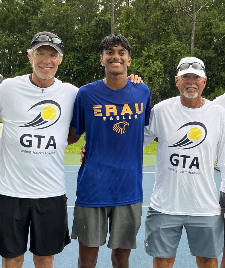 Three men smiling on a tennis court.